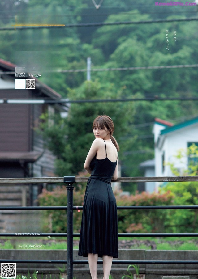 A woman in a black dress standing on a bridge.