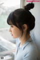 A woman looking out a window with her hair in a messy bun.