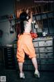 A woman in an orange jumpsuit standing in front of a wall of tools.