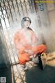 A woman in an orange jumpsuit sitting on the ground.