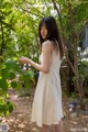 A woman in a white dress standing next to a tree.