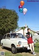 A woman holding a bunch of balloons in front of a car.