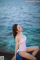 A woman in a white bathing suit sitting on a dock by the water.