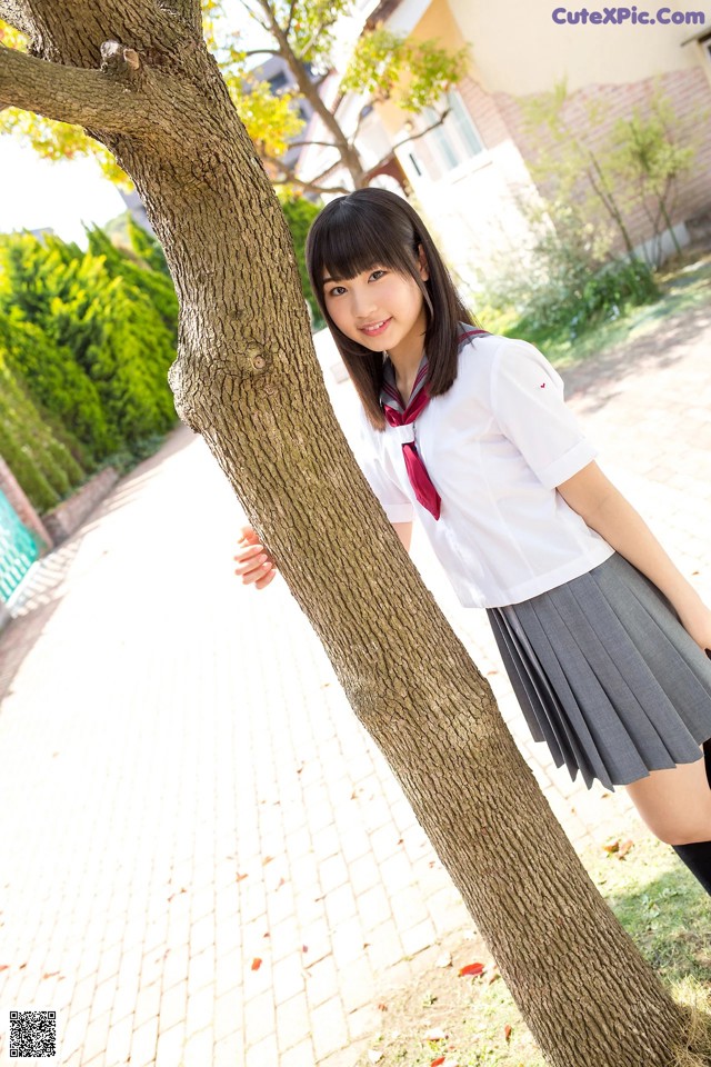 A woman in a school uniform leaning against a tree.