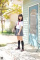 A woman in a school uniform standing in front of a house.