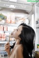 A woman eating a spoon in front of an open refrigerator.