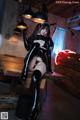 A woman in a black latex outfit sitting on a wooden table.