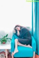 A woman sitting on a blue chair in front of a window.